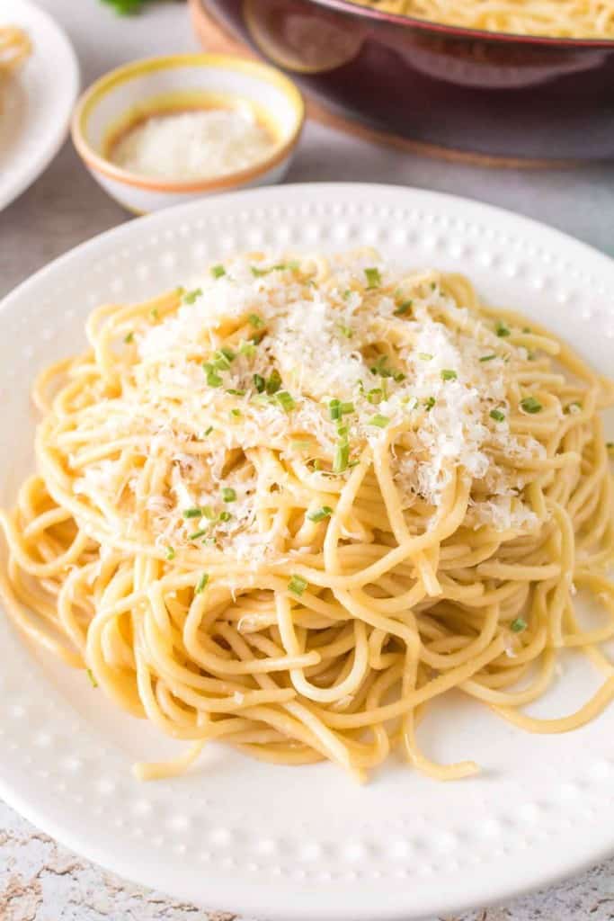 white plate of garlic noodle dinner with cheese and herbs on top