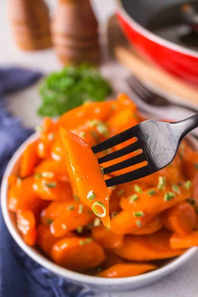 glazed carrots in a white dish with chives on top and one up close on a fork