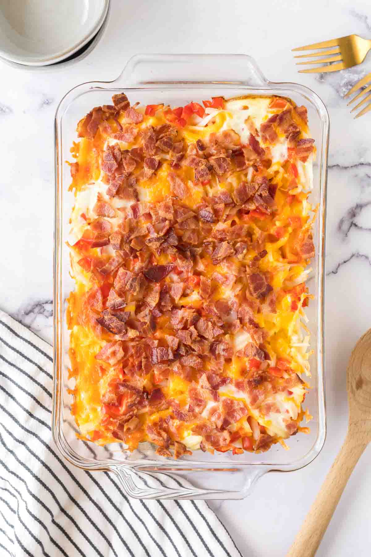baked in a clear rectangle baking dish, hash brown breakfast casserole with melted cheese and bacon on top