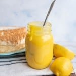 bright yellow lemon curd in a mason jar next to fresh lemons