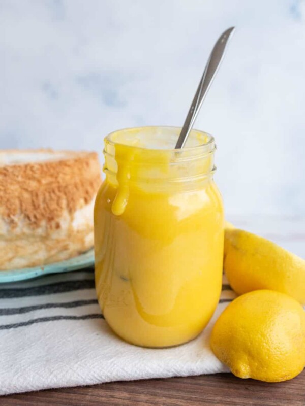 bright yellow lemon curd in a mason jar next to fresh lemons