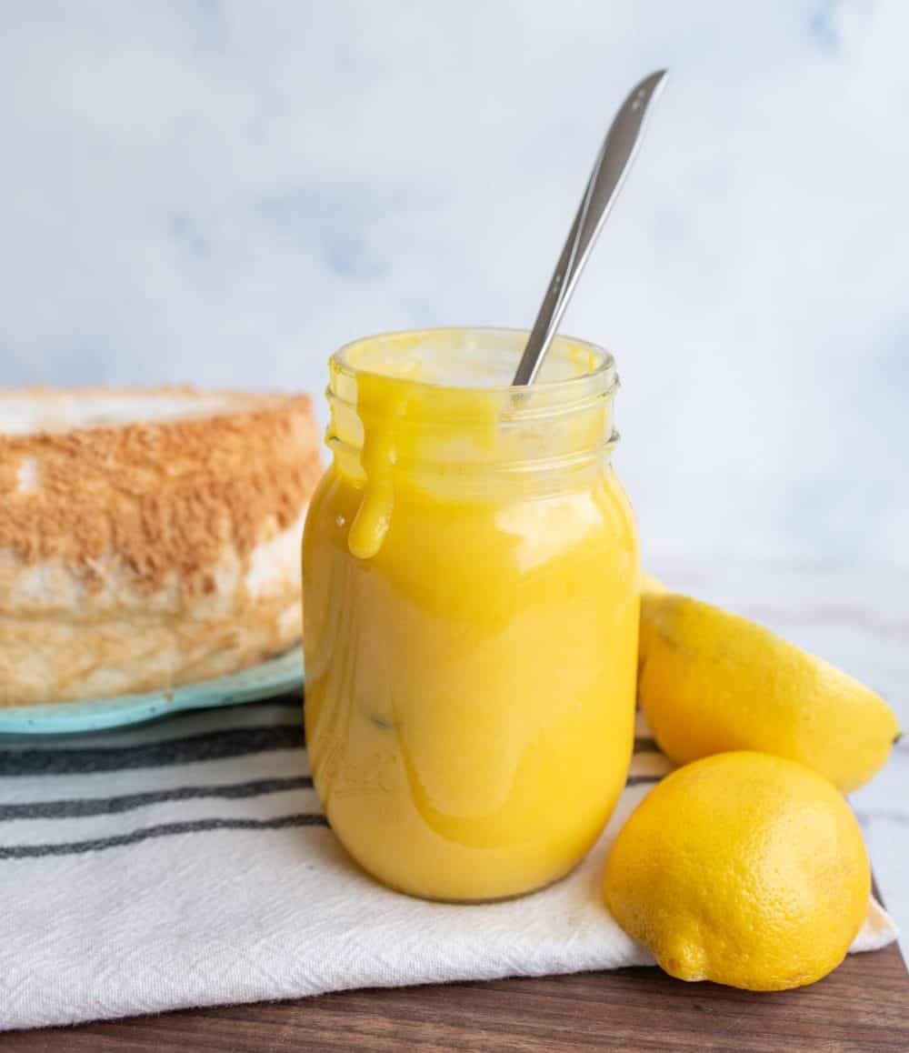 bright yellow lemon curd in a mason jar next to fresh lemons