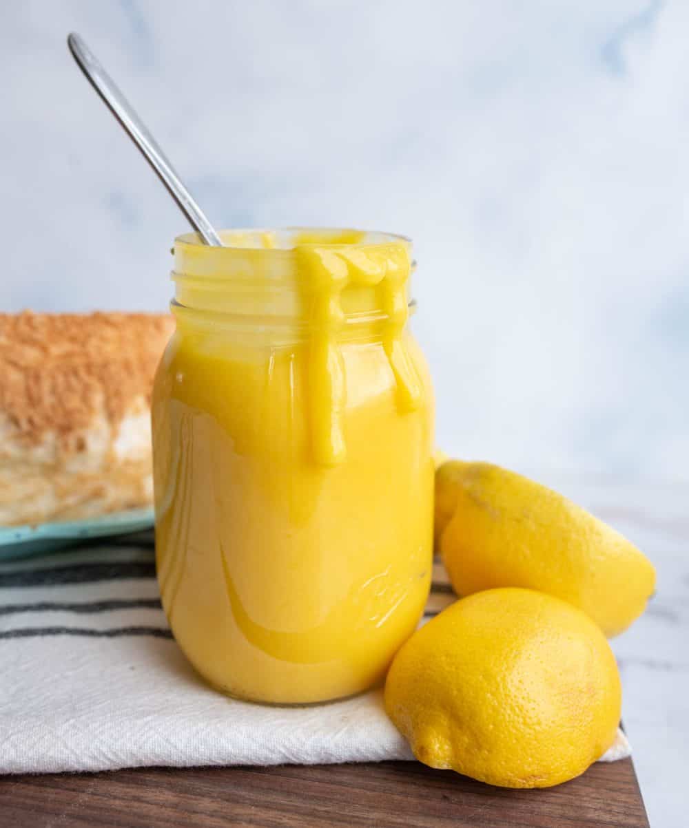 bright yellow lemon curd in a mason jar next to fresh lemons