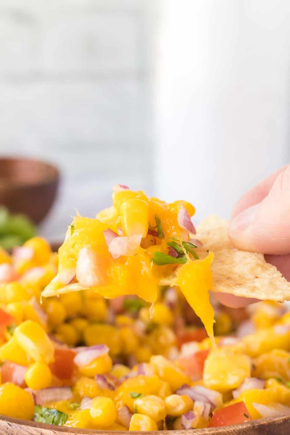 mango salsa in a wooden mixing bowl POV scooping with a tortilla chip