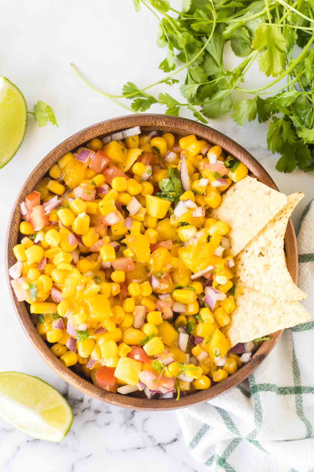 top view mango salsa in a wooden mixing bowl with chips in it