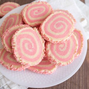 top view of a plate stacked with pink and tan swirl decorated pinwheel cookies with pink sprinkles