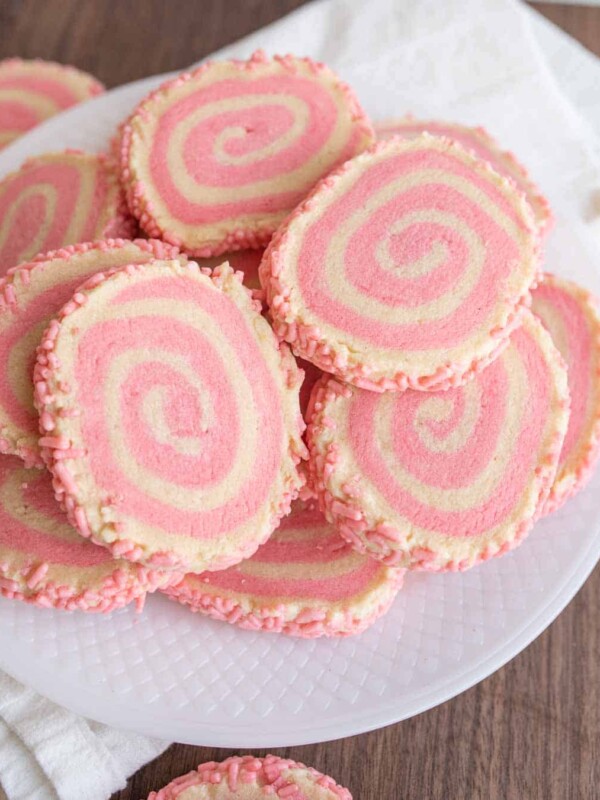 top view of a plate stacked with pink and tan swirl decorated pinwheel cookies with pink sprinkles