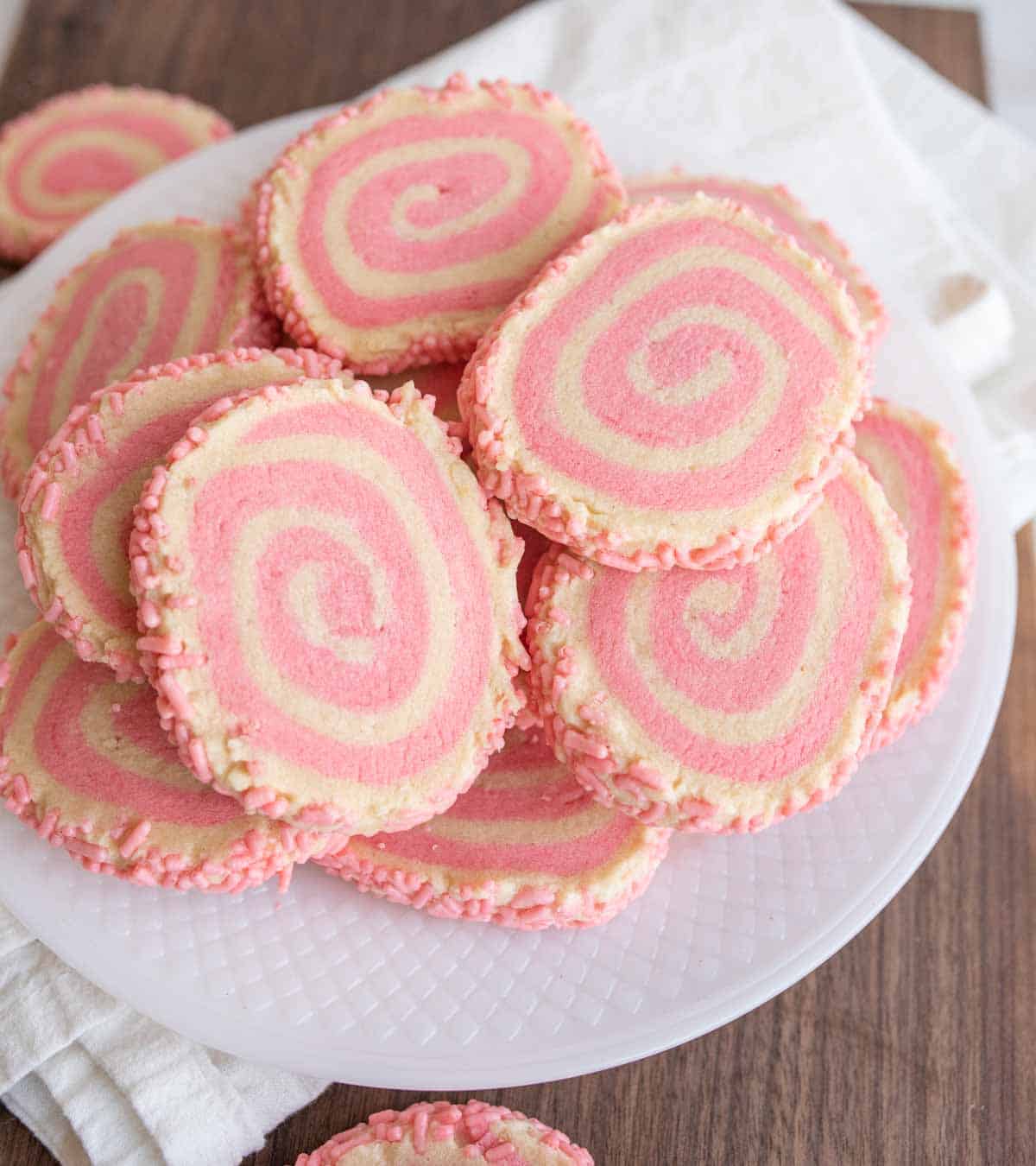 top view of a plate stacked with pink and tan swirl decorated pinwheel cookies with pink sprinkles