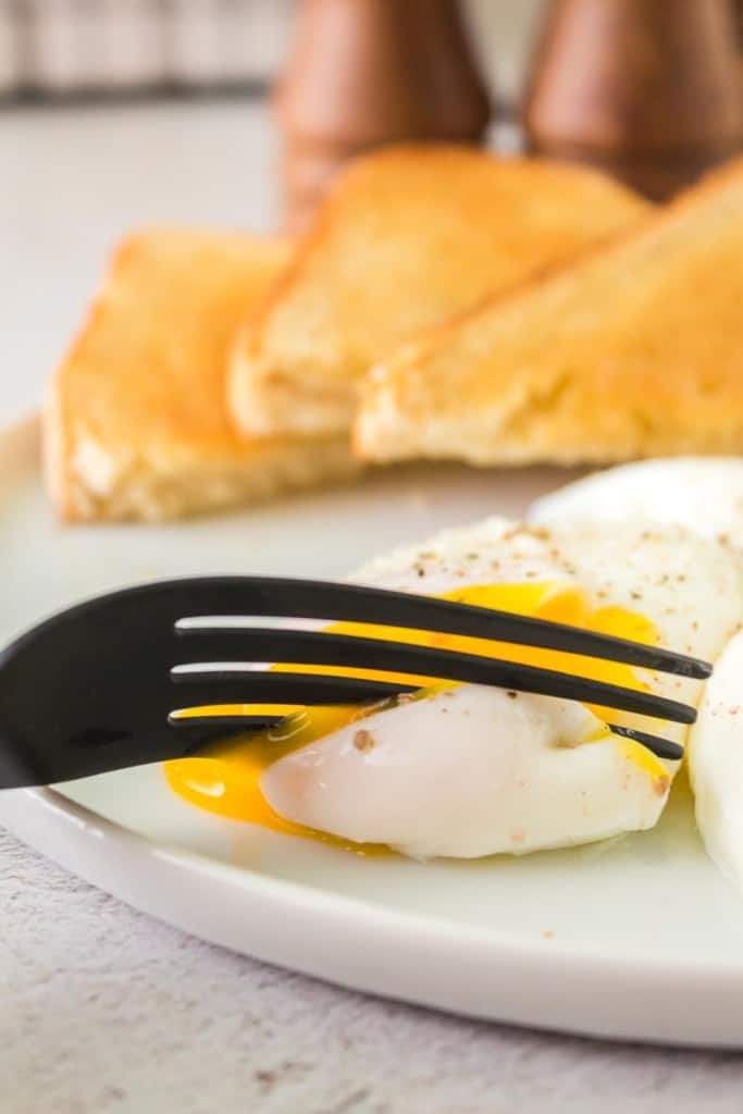 fork cutting a poached egg and its yolk gooing out