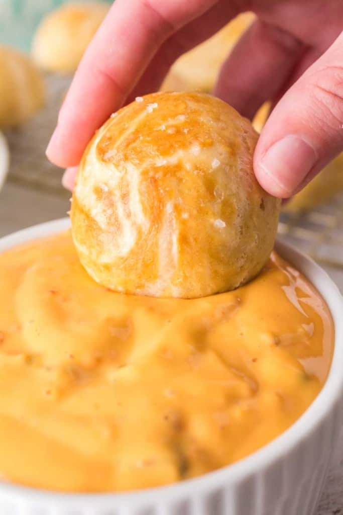 Pretzel bite being dipped into cheese sauce.