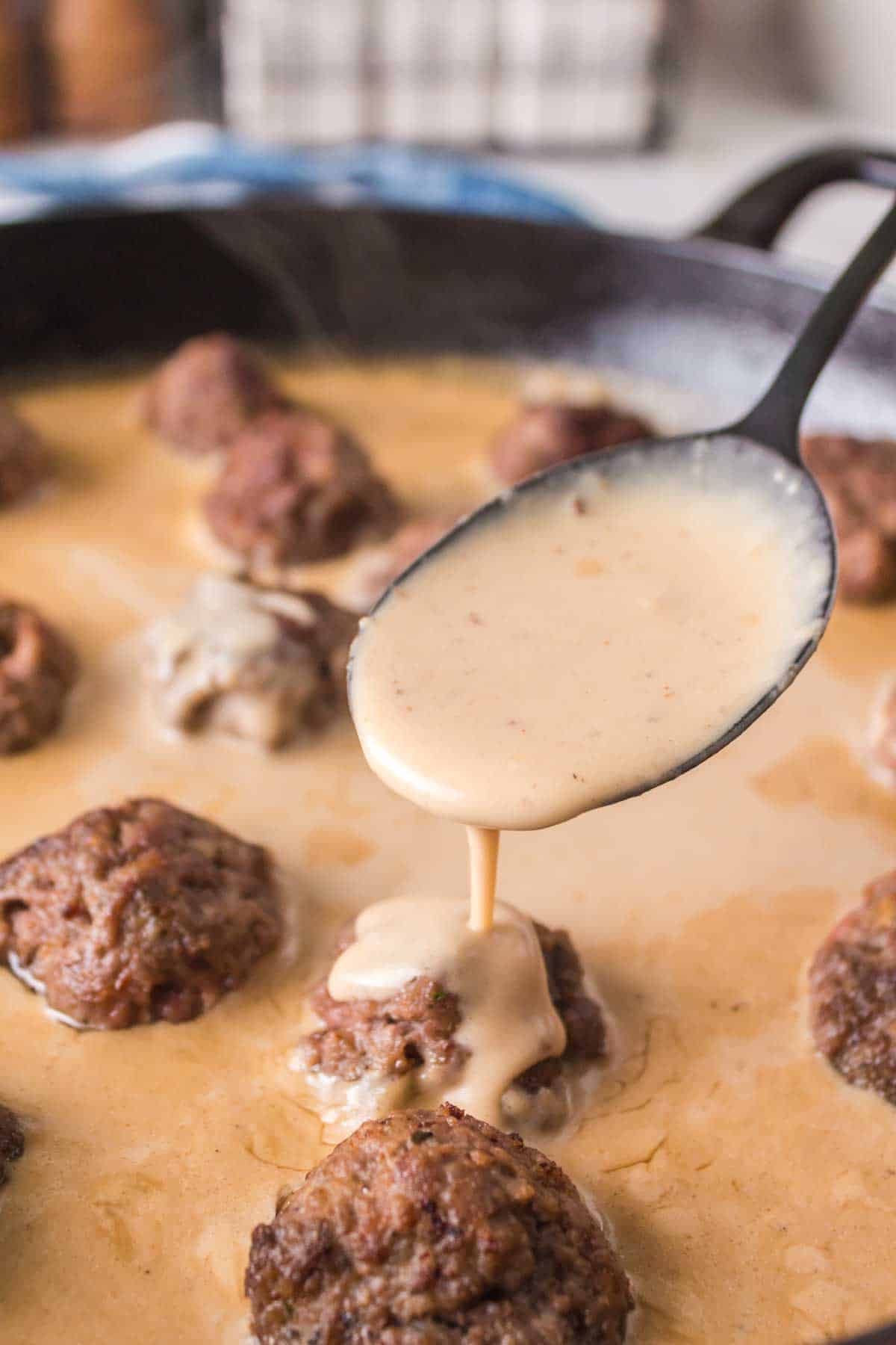 swedish meatball sauce poured over meatballs in cast iron pan