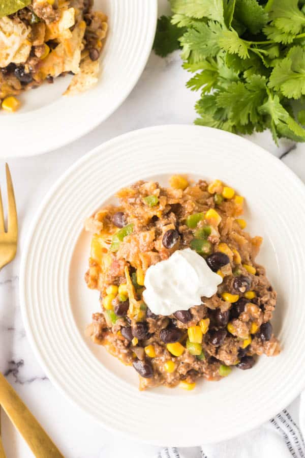 two white plate os taco casserole with sour cream on top