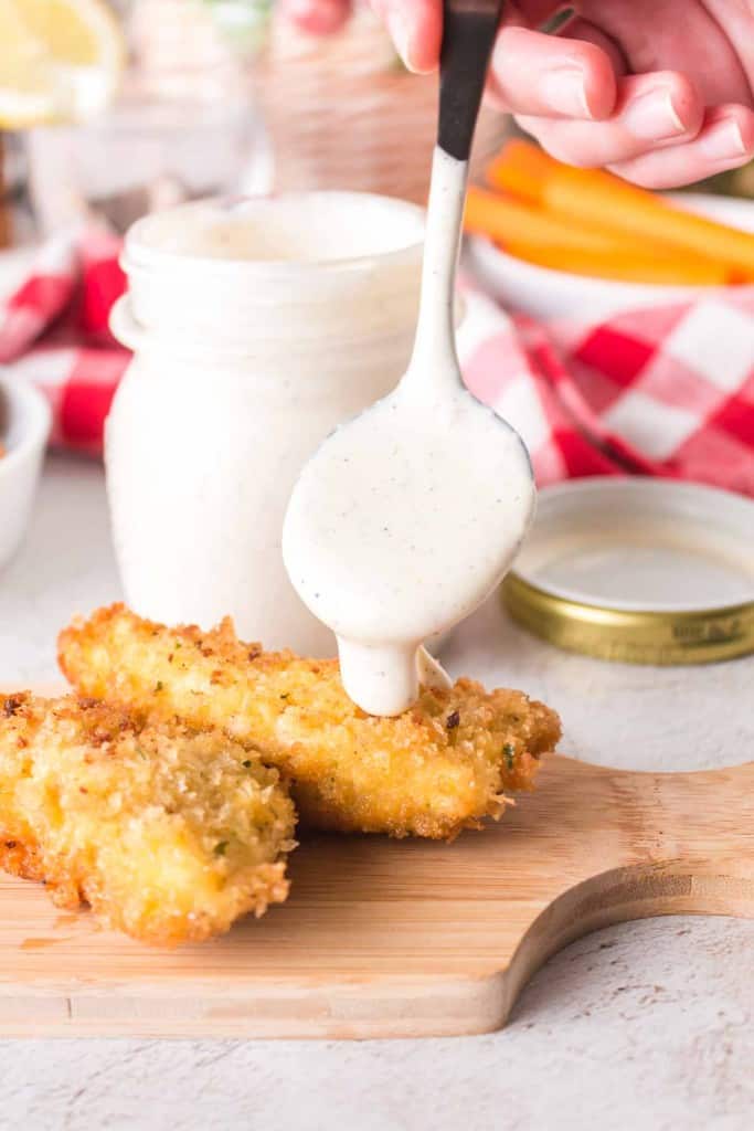 White BBQ sauce getting dripped on chicken tender.