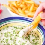 POV dipping fries into a small bowl of aioli with chives on top