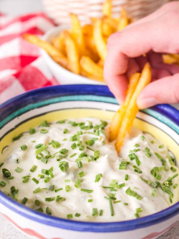 POV dipping fries into a small bowl of aioli with chives on top