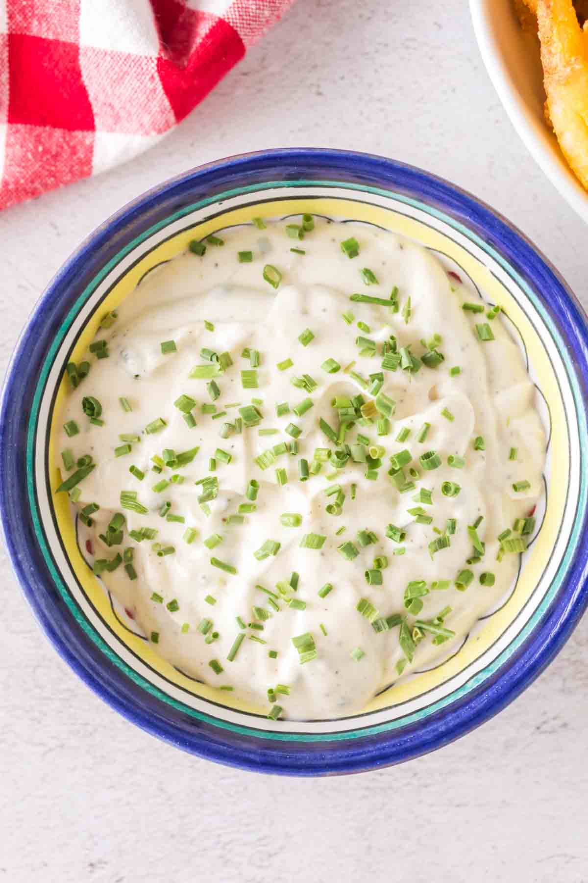 POV dipping fries into a small bowl of aioli with chives on top