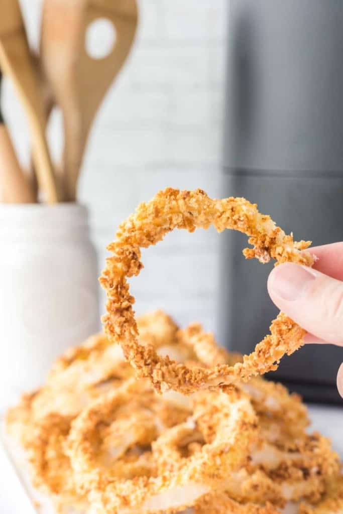 POV hand holding a circle crispy breaded and baked onion ring