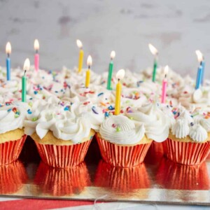 vanilla cupcakes with white icing and rainbow sprinkles for birthday cupcakes with a candle in each