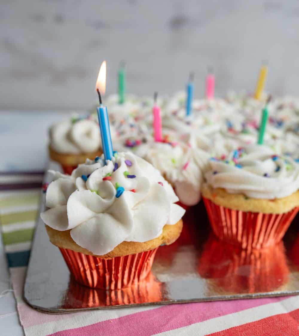 vanilla cupcakes with white icing and rainbow sprinkles for birthday cupcakes with a candle in each