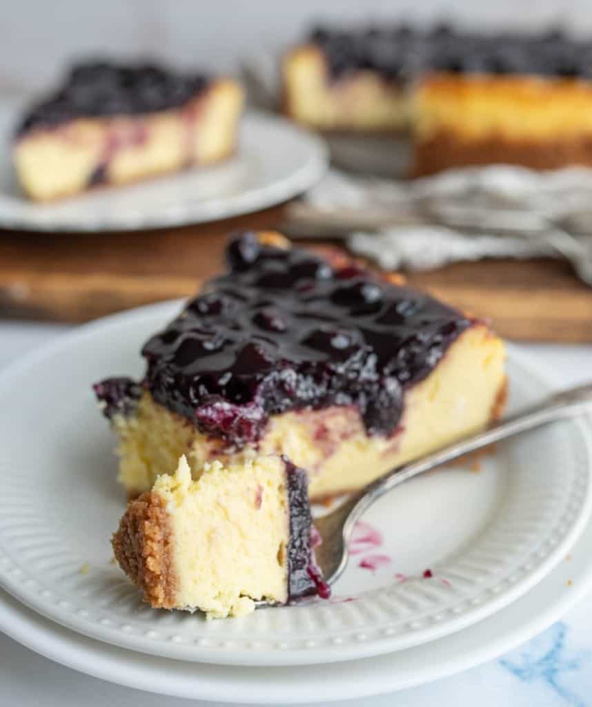 one slice portioned from a whole blueberry cheesecake and a fork full of a bite ready to eat