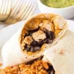 chicken burritos sliced in half with black beans with rice on a white plate close up