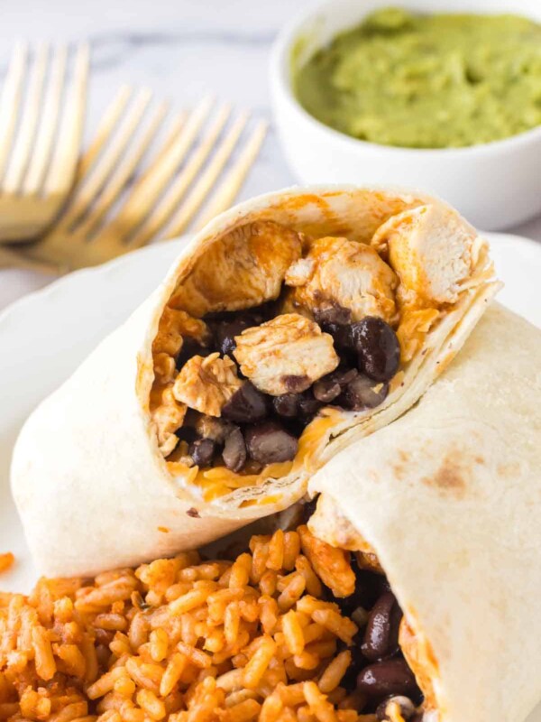 chicken burritos sliced in half with black beans with rice on a white plate close up