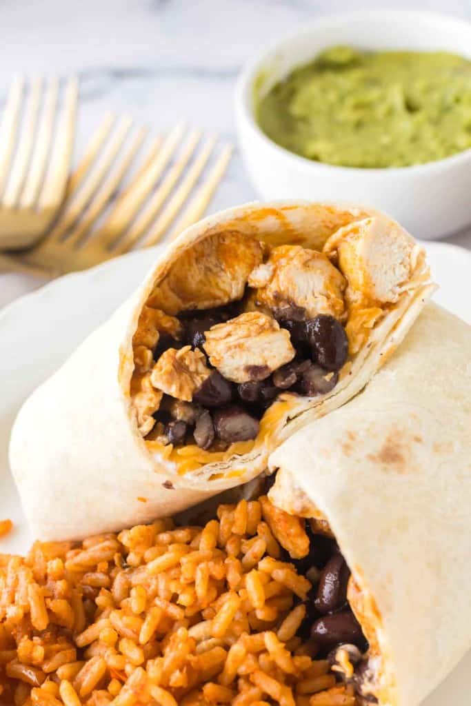 chicken burritos sliced in half with black beans with rice on a white plate close up