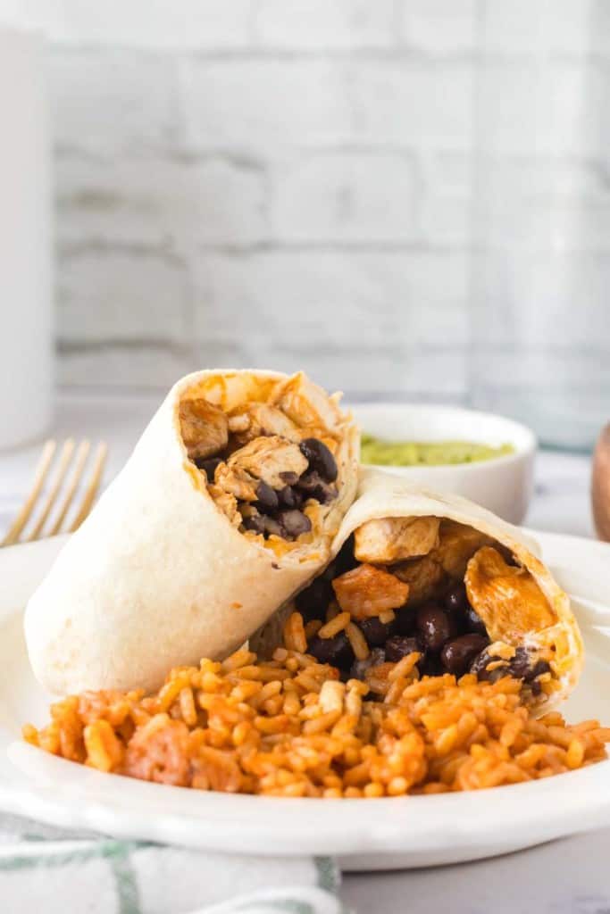 chicken burritos sliced in half with black beans with rice on a white plate