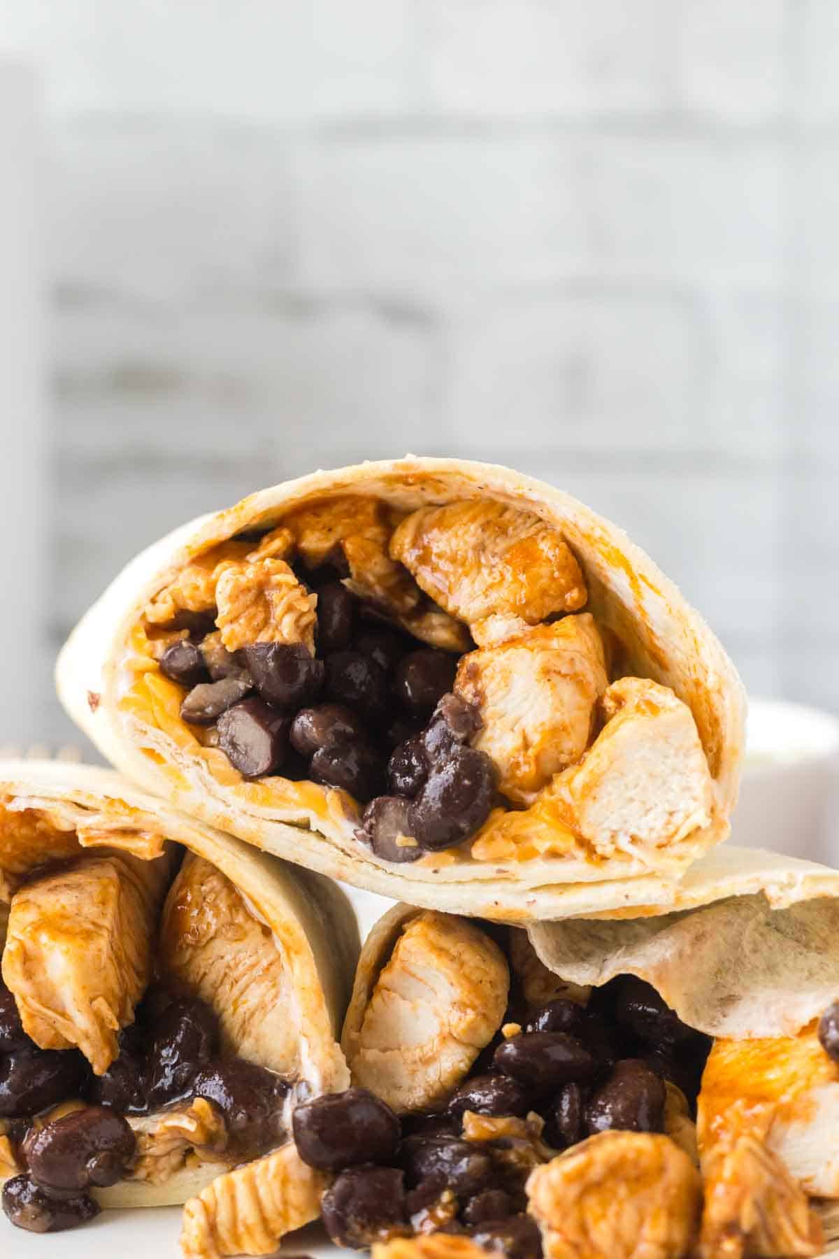 close up chicken burritos sliced in half with black beans with rice on a white plate