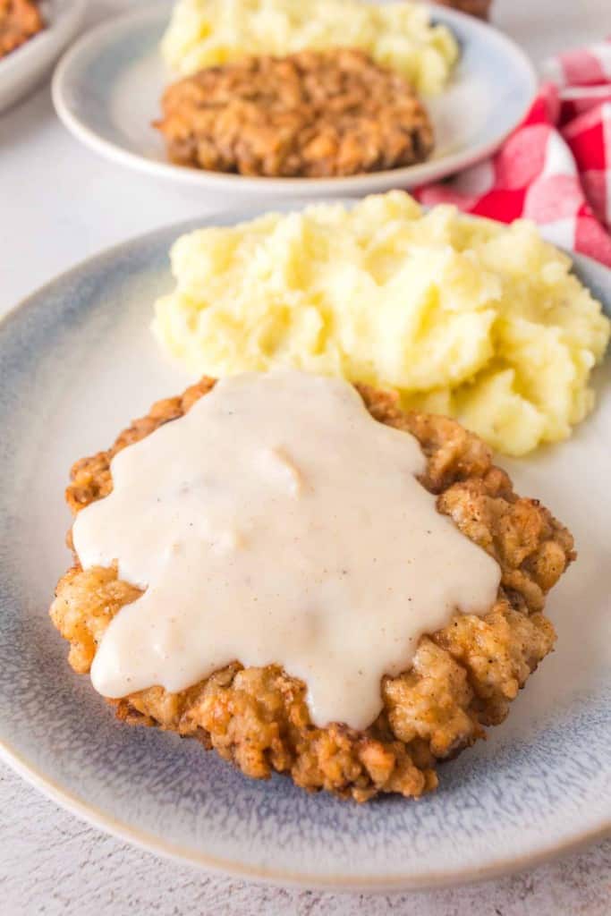 crispy chicken fried steak on a plate with gravy on top and mashed potatoes