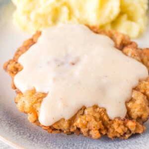 crispy chicken fried steak on a plate with gravy on top and mashed potatoes