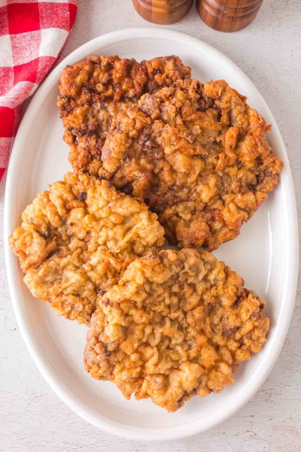 three crispy golden chicken fried steak pieces on a white plate