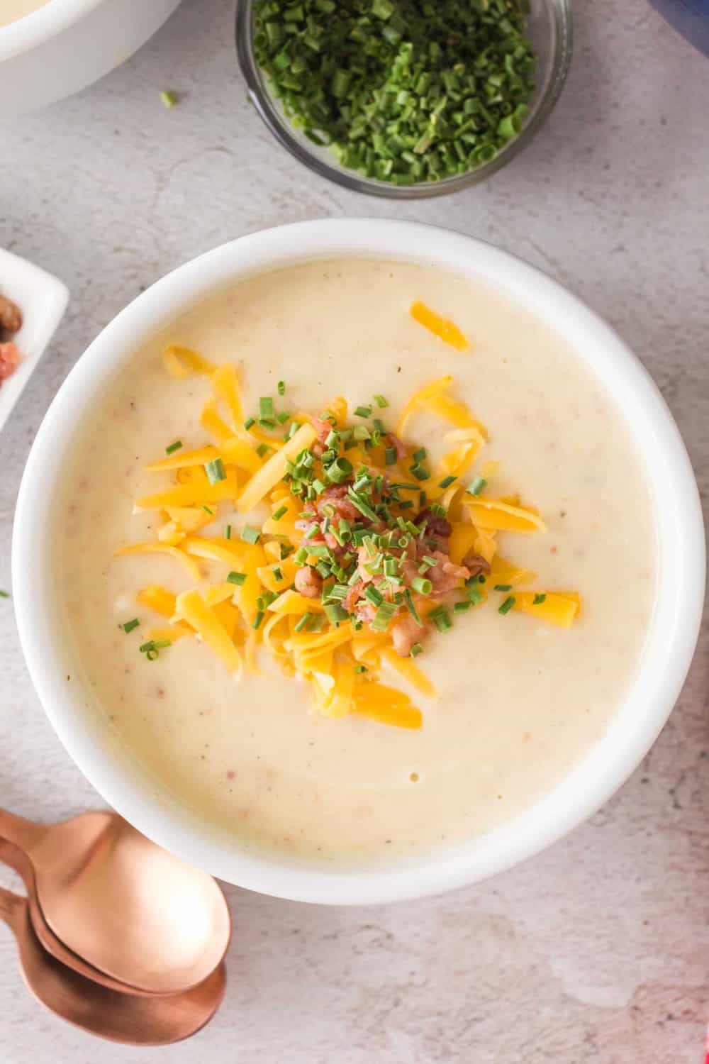 top view of a bowl of cream of potato soup with cheese bacon and chives on top