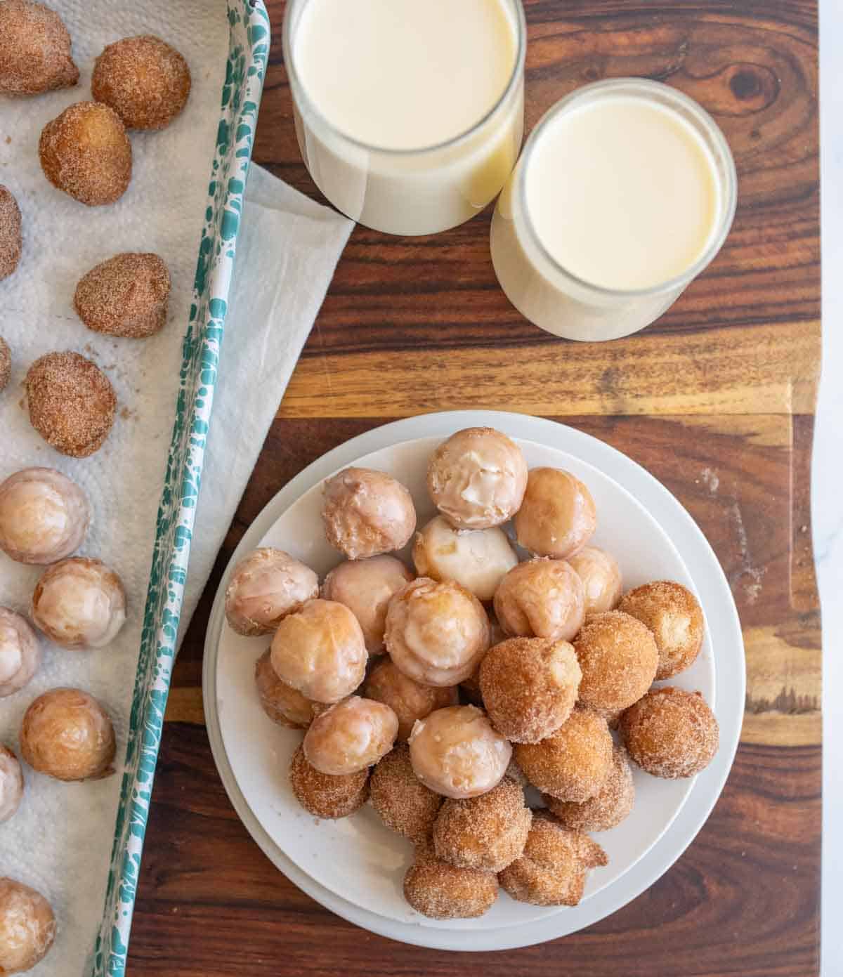top view of a plate stacked with round iced and sugar donut hole bites with glasses of milk