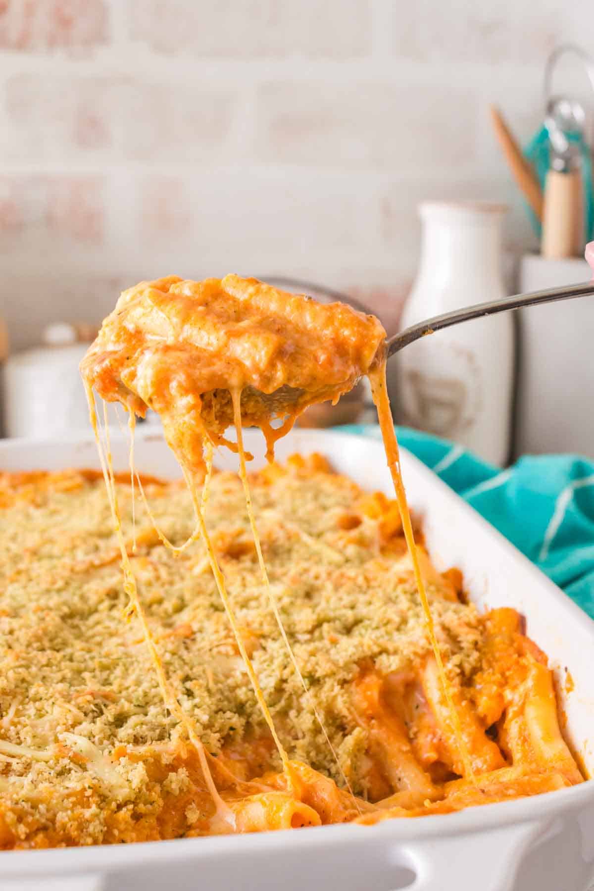 five cheese zita forno pasta with a creamy red sauce in a white baking dish being spooned out