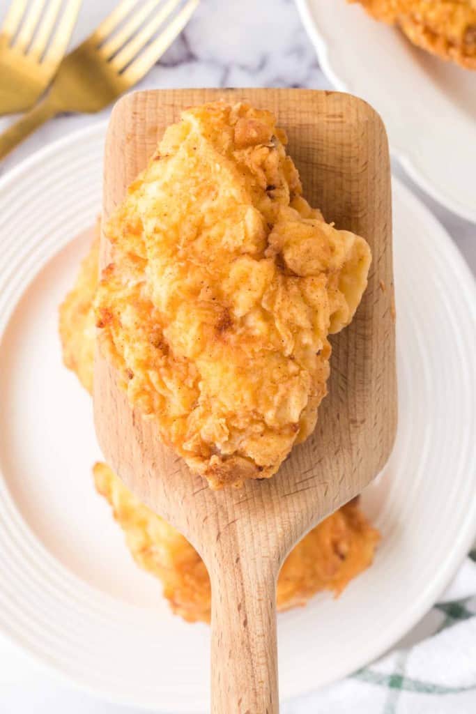 golden and crisp perfectly fried chicken scooped on a wooden spatula top view