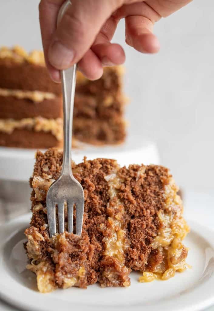 one slice with a POV fork getting a bite of three layered round german chocolate cake with traditional coconut frosting