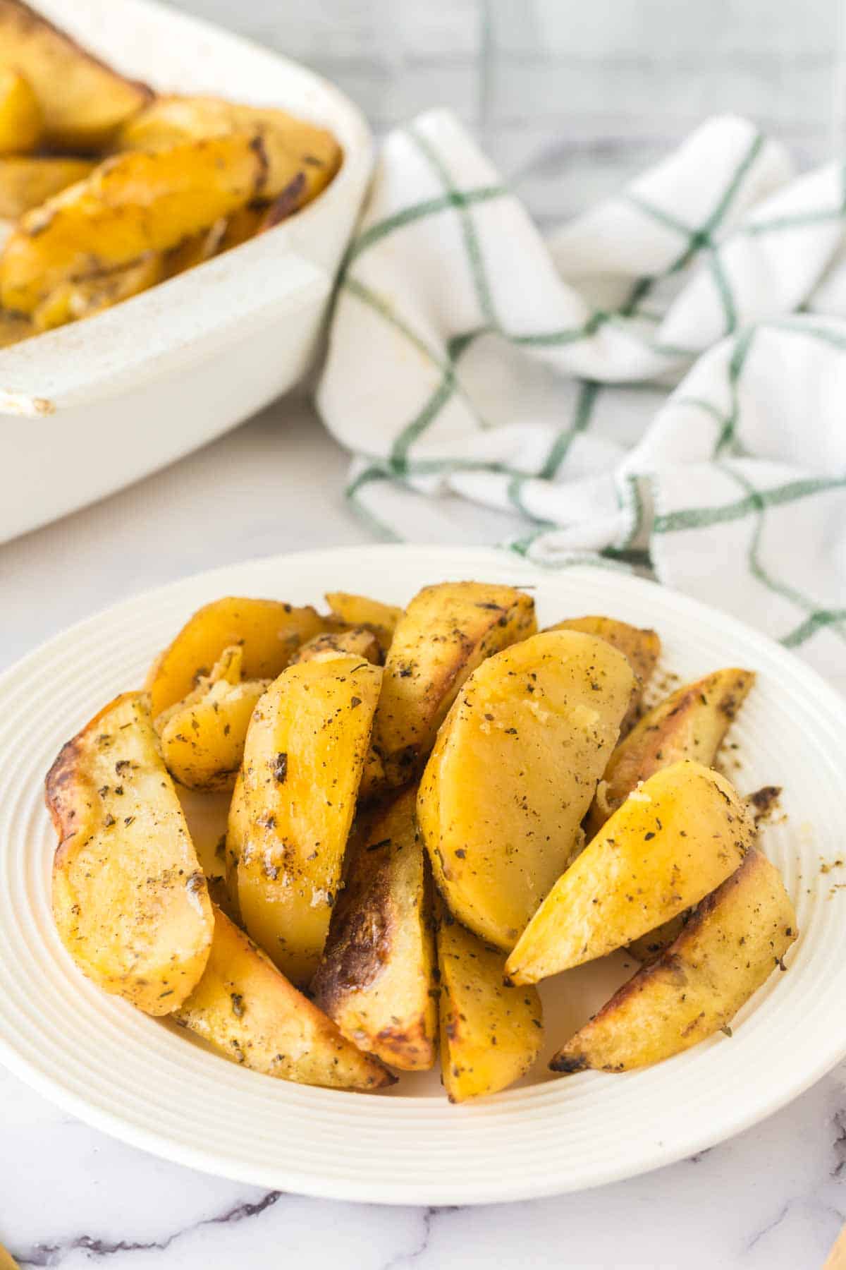 white plate of greek potatoes cut in wedges and seasoned