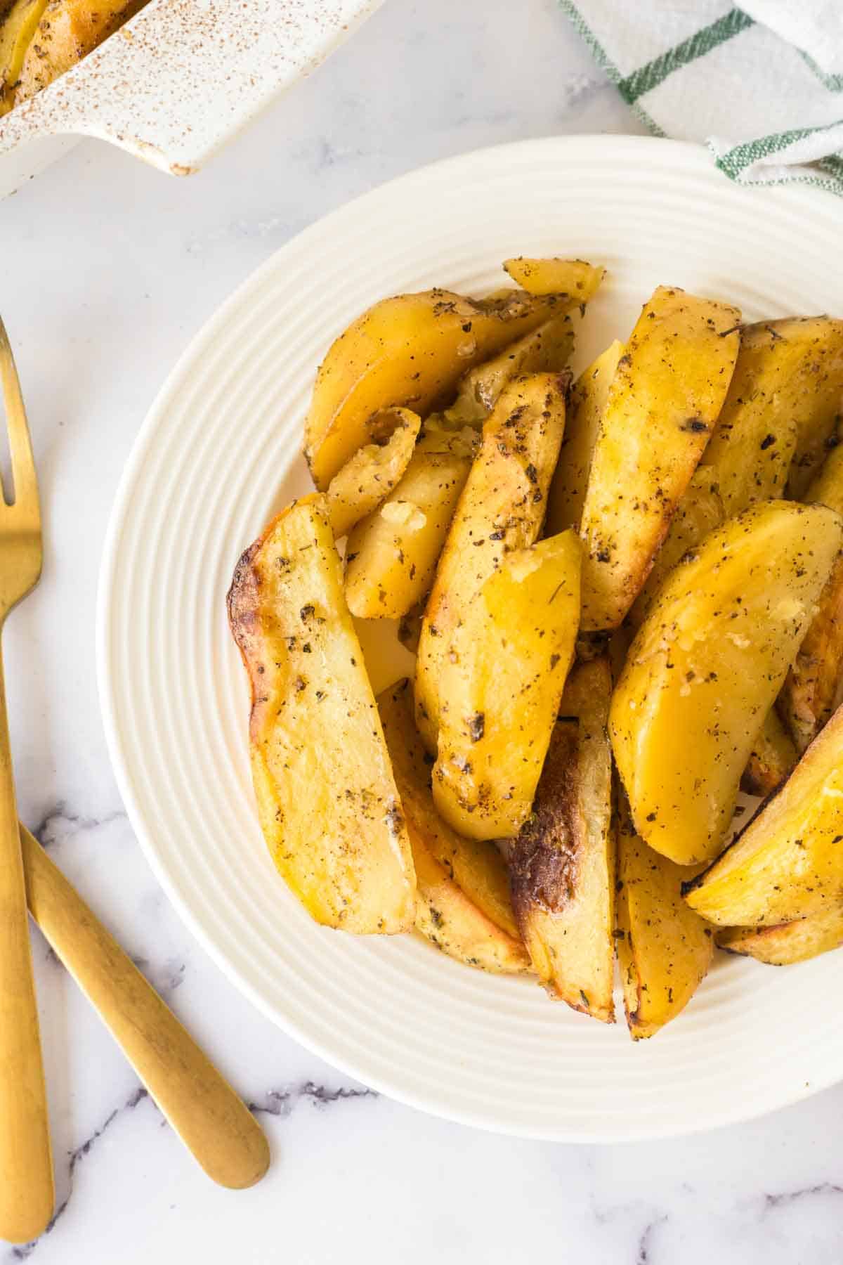 white plate of greek potatoes cut in wedges and seasoned