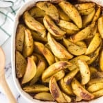 baking dish of greek potatoes cut in wedges and seasoned