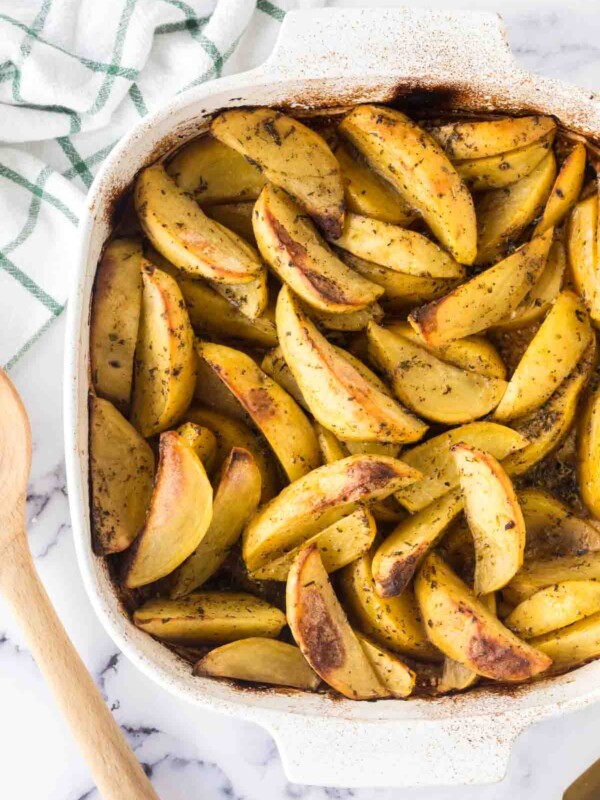 baking dish of greek potatoes cut in wedges and seasoned