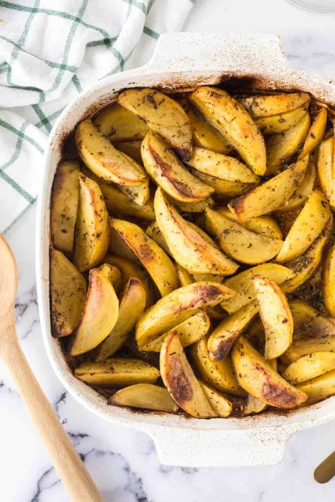 baking dish of greek potatoes cut in wedges and seasoned