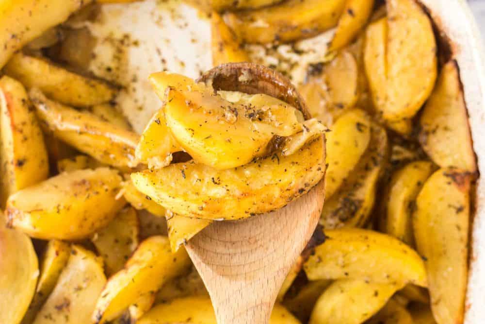 close up of a spoonful of greek potatoes cut in wedges and seasoned