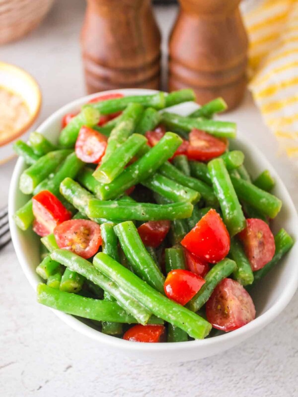 a white bowl of green bean salad with tomatoes
