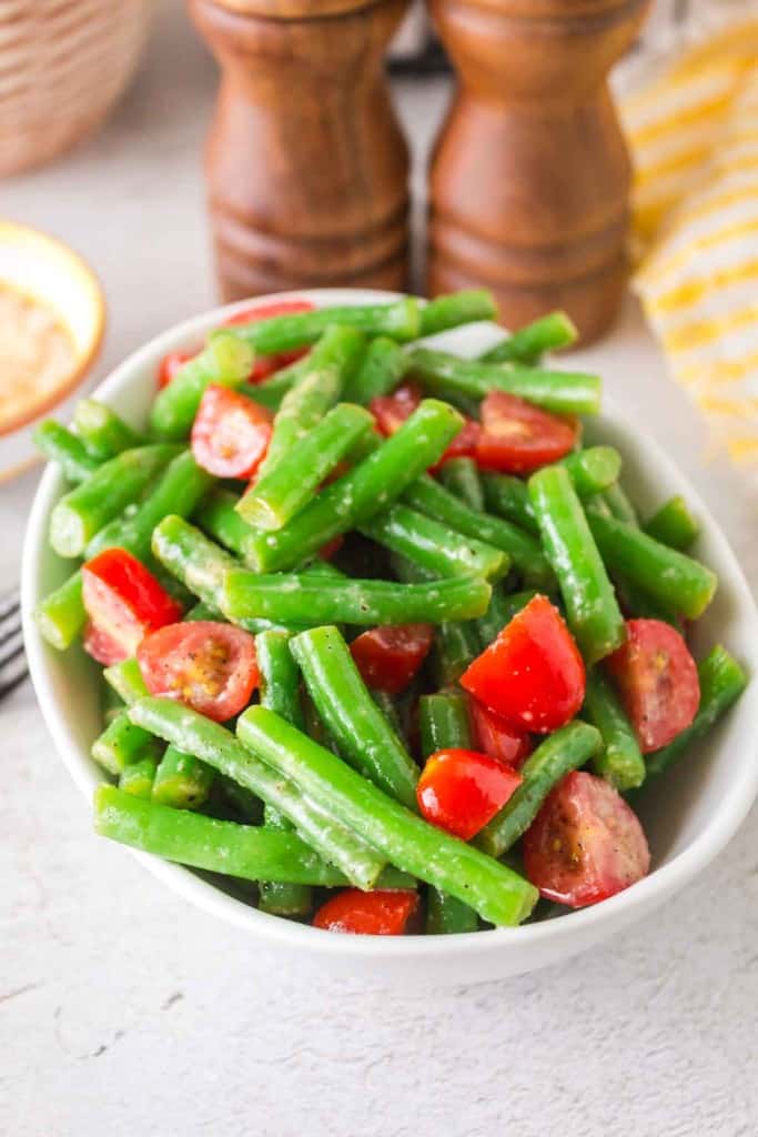 a white bowl of green bean salad with tomatoes