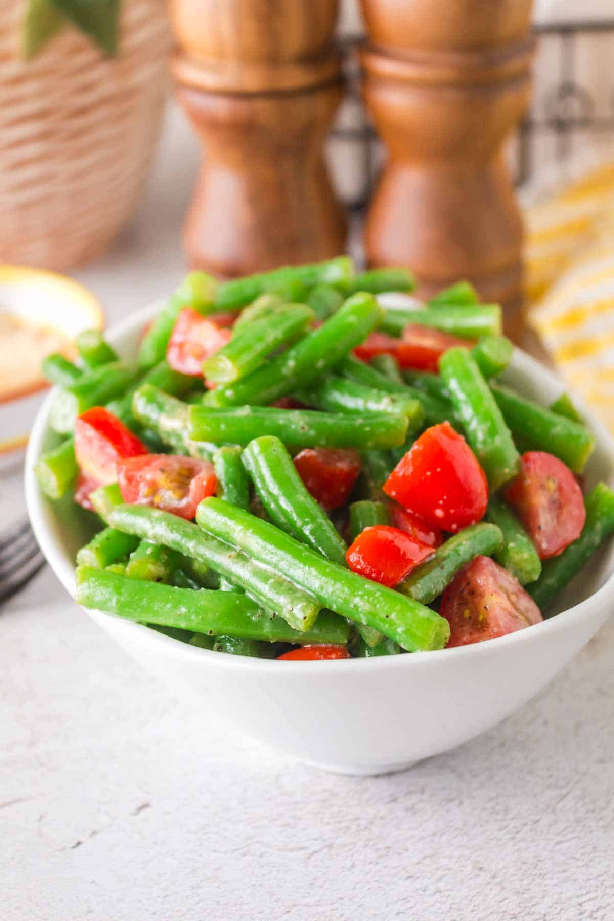 a white bowl of green bean salad with tomatoes