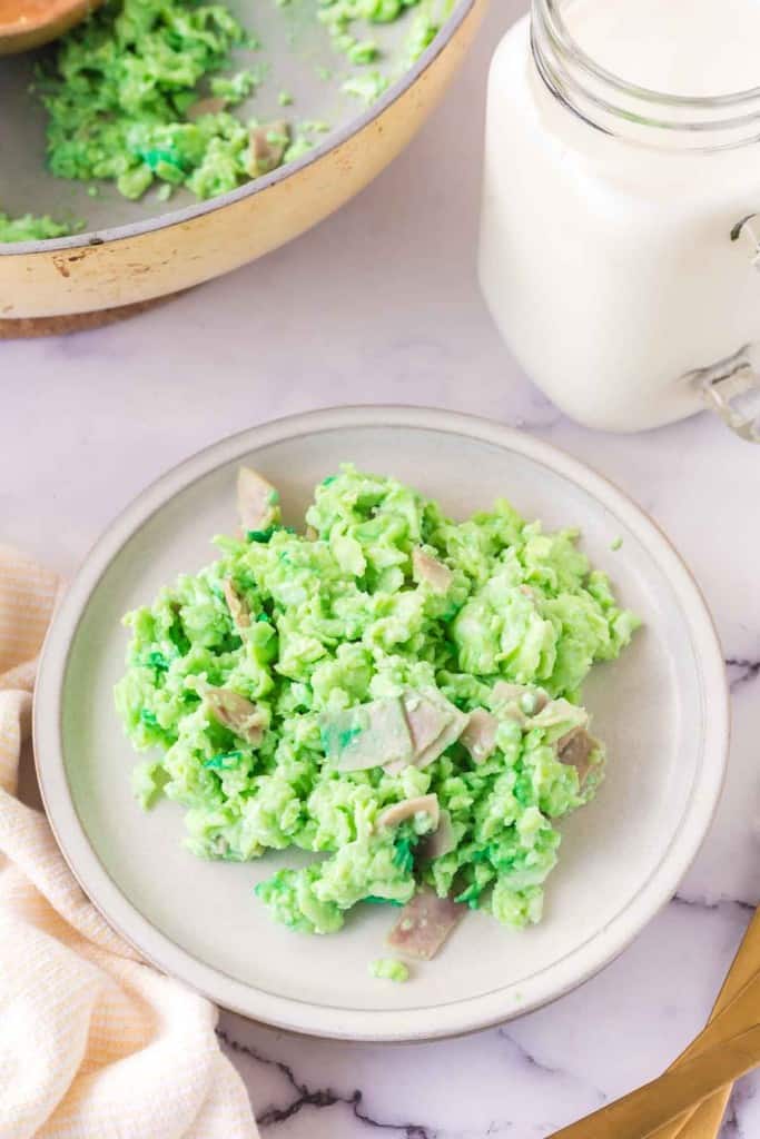 green colored scrambled eggs with pieces of ham on a white plate