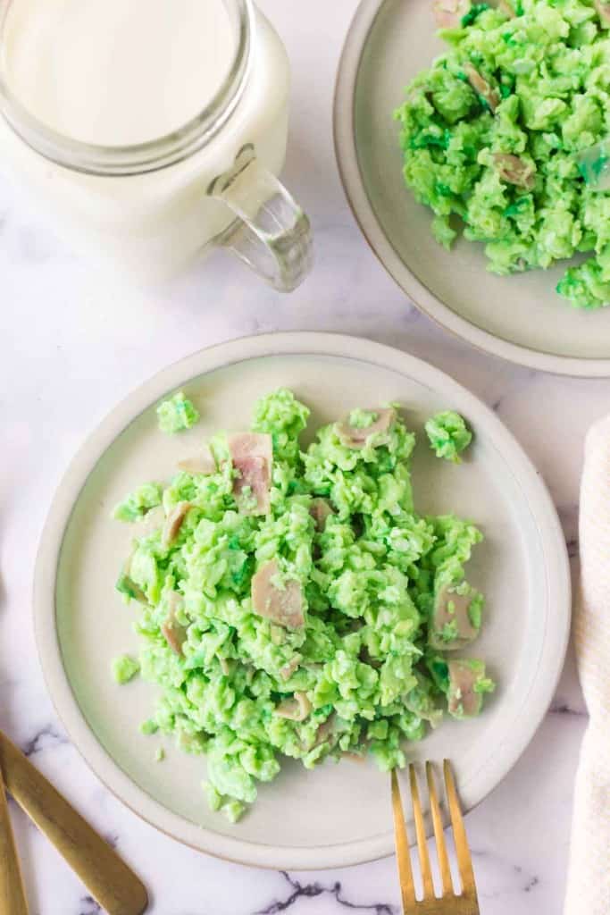 top view of green colored scrambled eggs with pieces of ham on a white plate