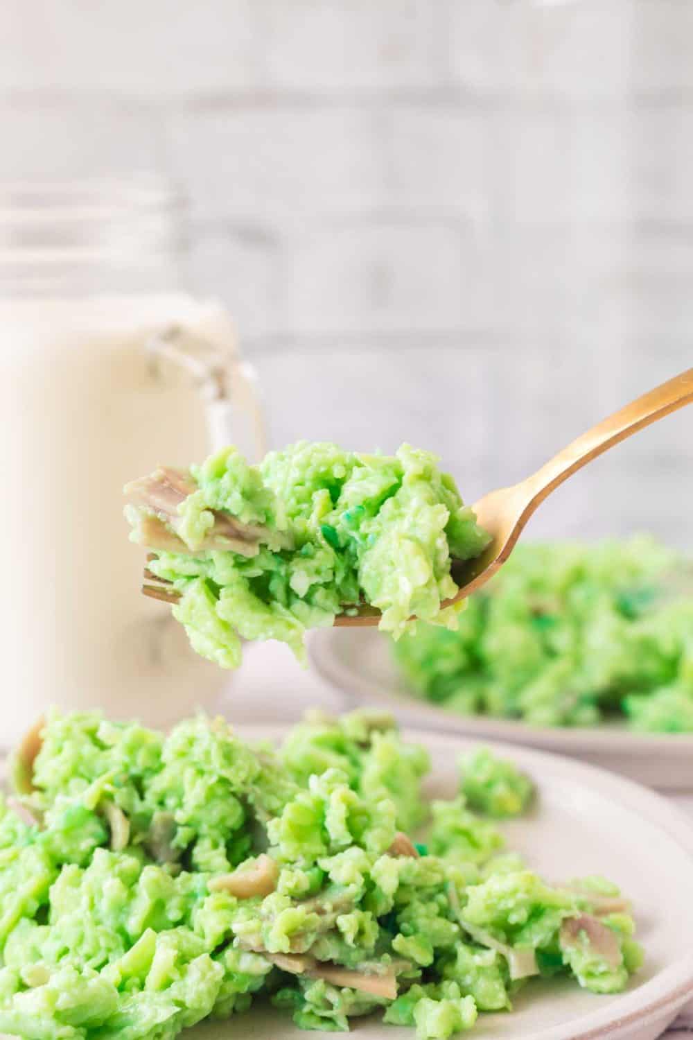 green colored scrambled eggs with pieces of ham on a white plate with a side view of a fork-full