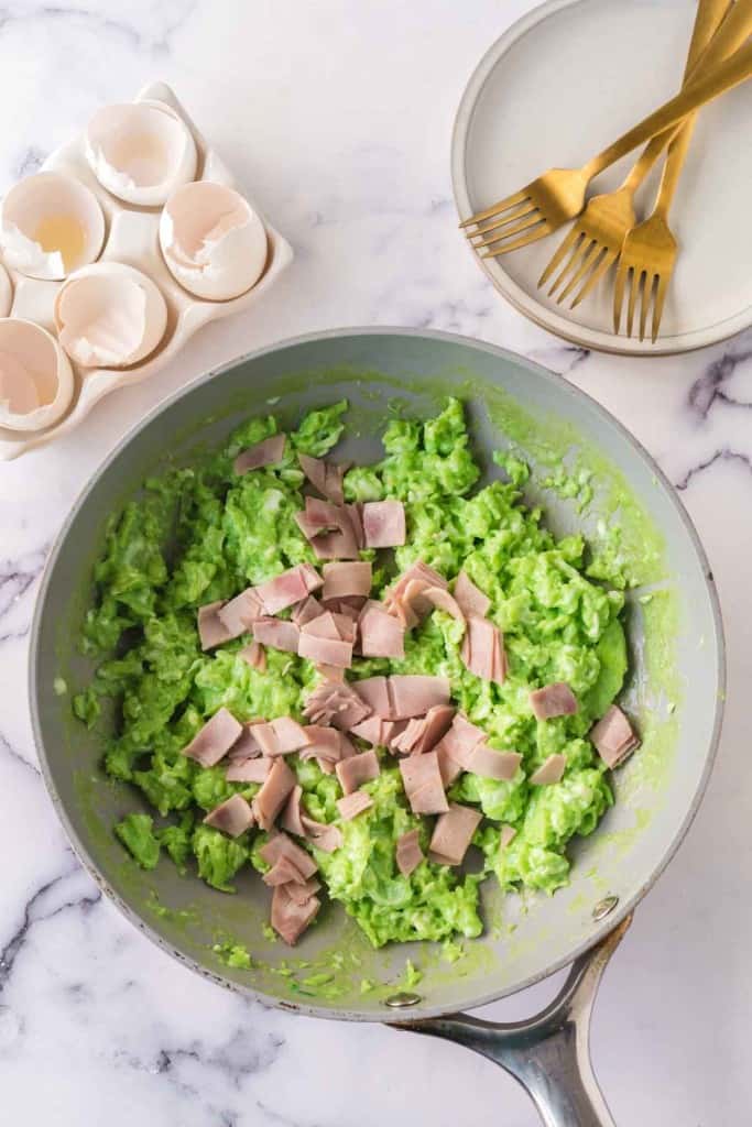green colored scrambled eggs with pieces of ham in a pan
